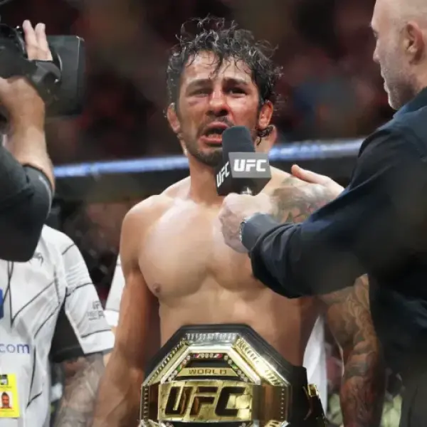 Un combattant de MMA au visage meurtri tient une ceinture de champion de l'UFC. Un micro est levé pour une interview d'après-combat, dans une ambiance intense.