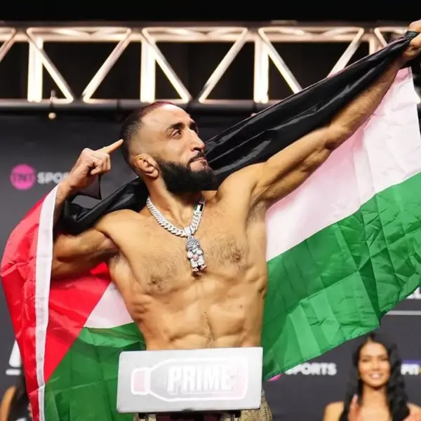 Un homme musclé pose avec assurance, drapé dans le drapeau palestinien, sur une scène sportive. Il pointe vers le haut, dégageant fierté et détermination.