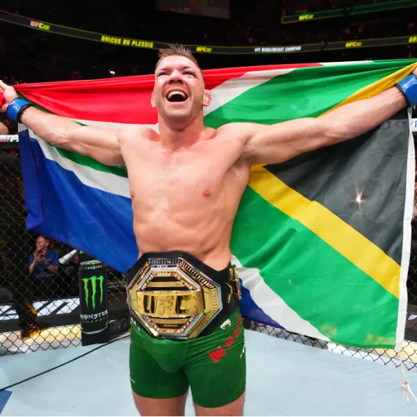 Un combattant de MMA triomphant se tient sur le ring, brandissant le drapeau sud-africain. Vêtu d'un short vert et d'une ceinture de champion de l'UFC, il respire la joie et la victoire.