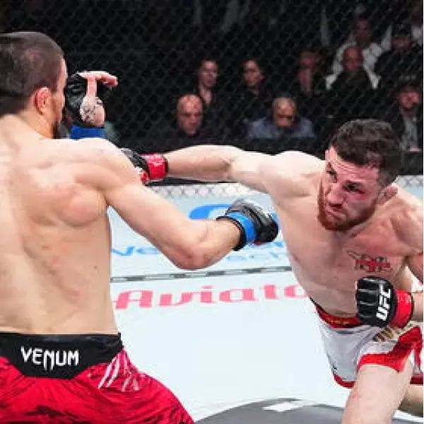 Deux combattants de MMA s'affrontent dans une cage. L'un assène un coup puissant, tandis que l'autre se défend, affichant concentration et détermination. Le public en arrière-plan.