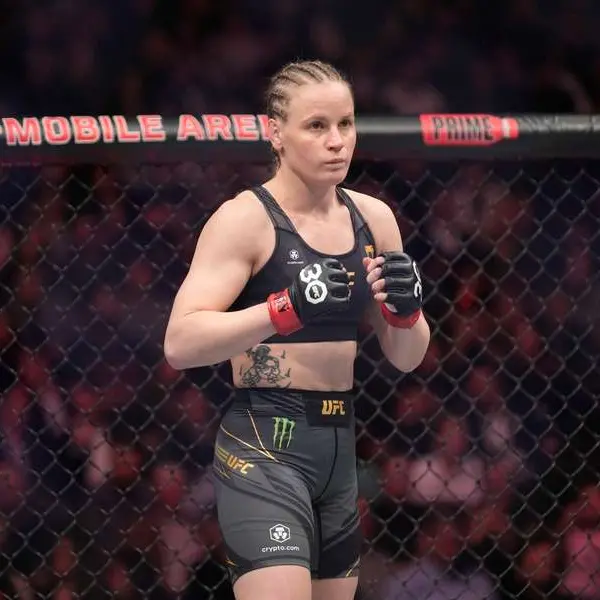 Une combattante de MMA aux cheveux tressés et à l'équipement noir se tient dans une cage octogonale. Son expression concentrée respire l'intensité et la préparation.