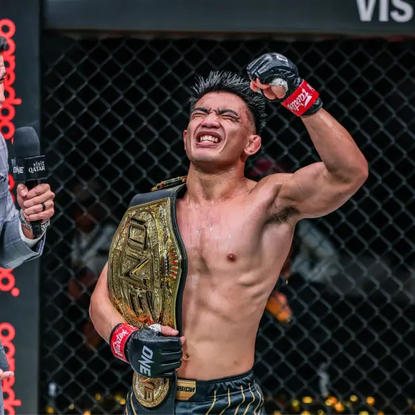 Un artiste martial mixte victorieux, portant des gants de boxe, célèbre avec une ceinture de championnat sur son épaule dans une cage octogonale, rayonnant de joie.
