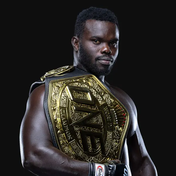 Un artiste martial mixte pose avec assurance avec une grande ceinture de championnat en or sur son épaule, sur un fond noir uni.